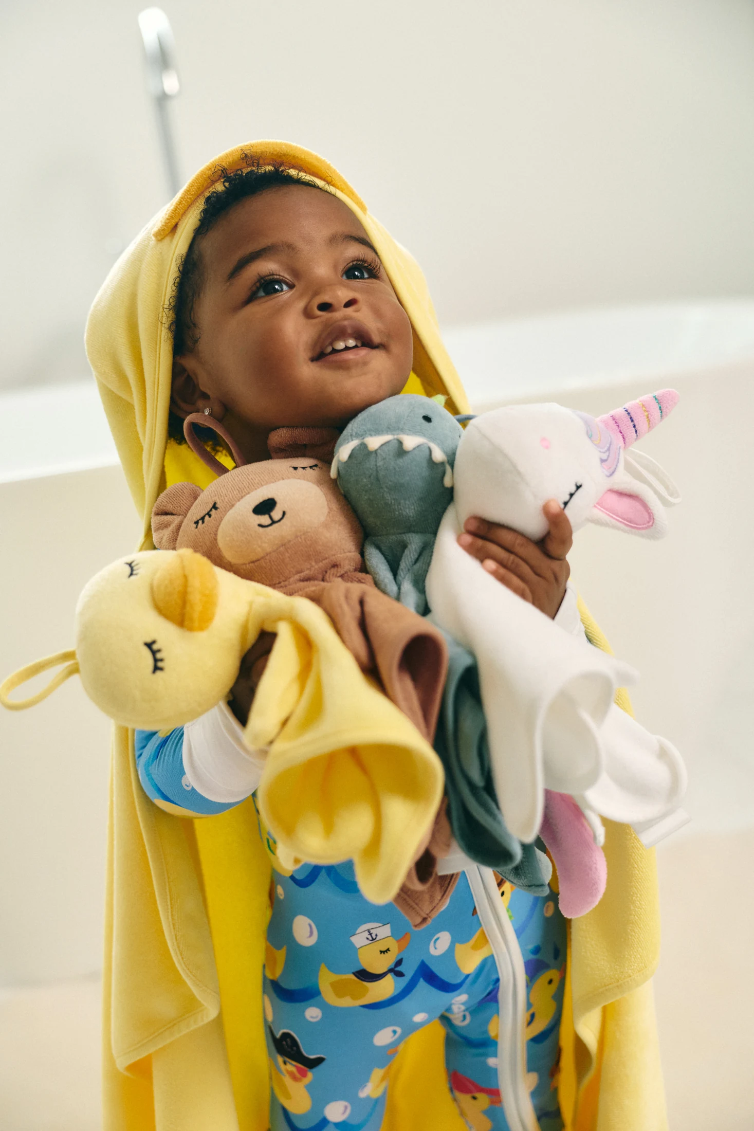 Child in yellow holding a collection of stuffed animals