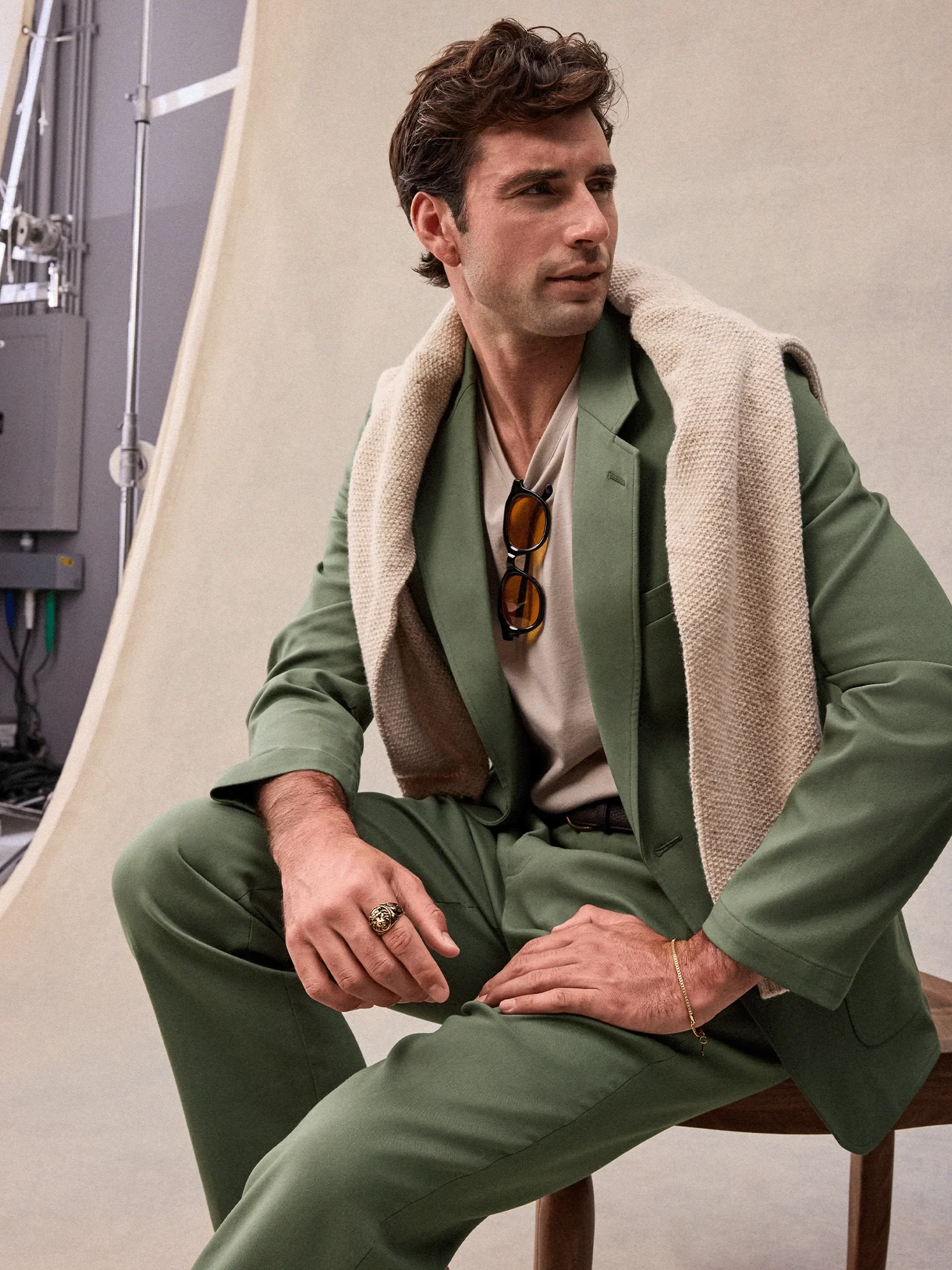 Seated man in a green suit with knitwear draped over his shoulders